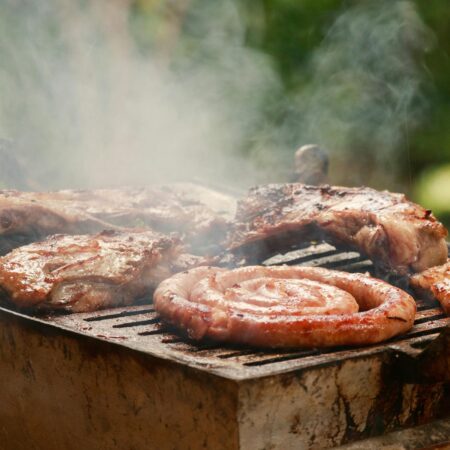 A sizzling BBQ grill with meat and sausages smoking outdoors, perfect for summer cookouts.